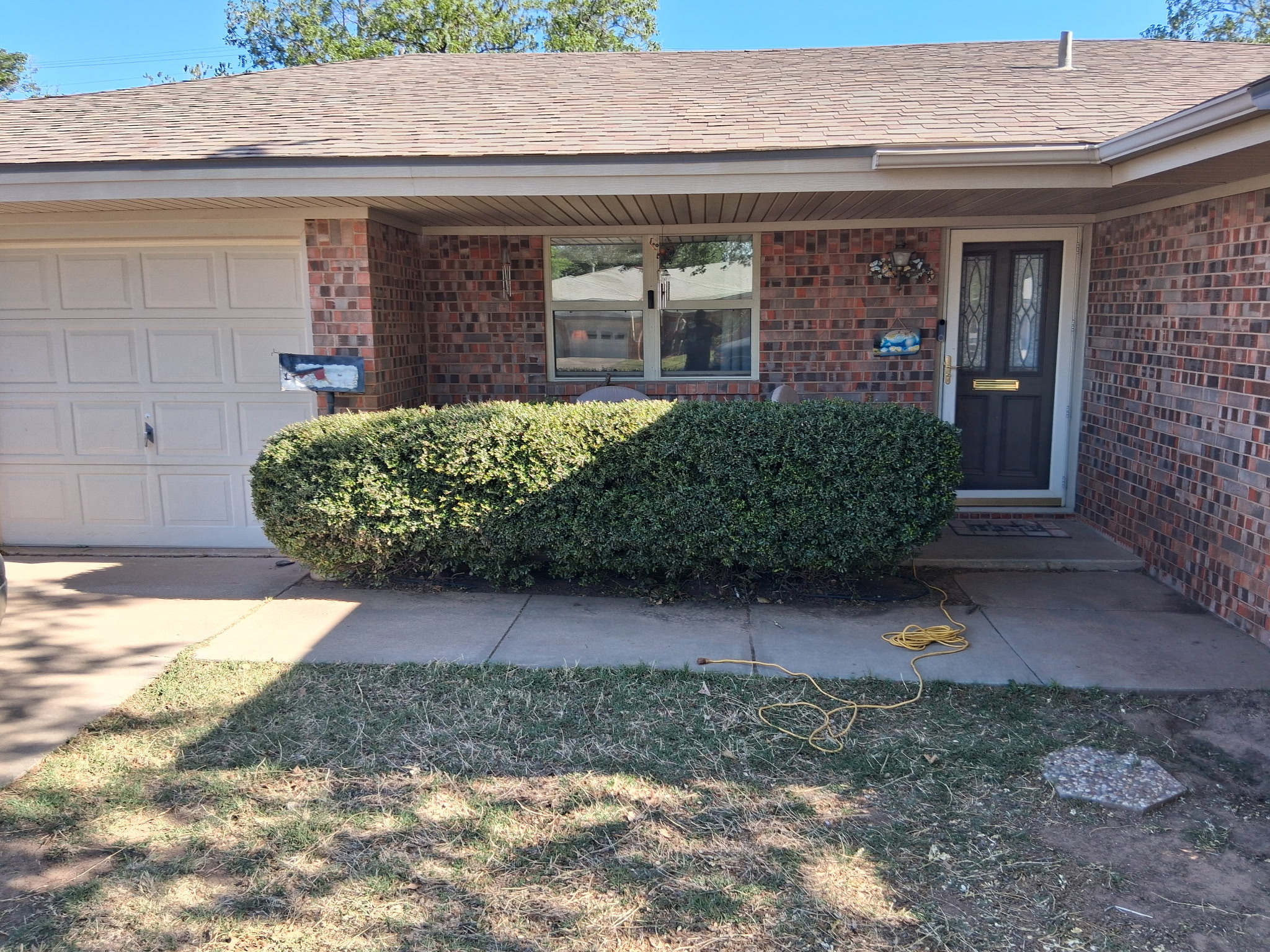 Overgrown boxwood hedge at a brick home before trimming by 3D Landscaping in Lubbock, TX