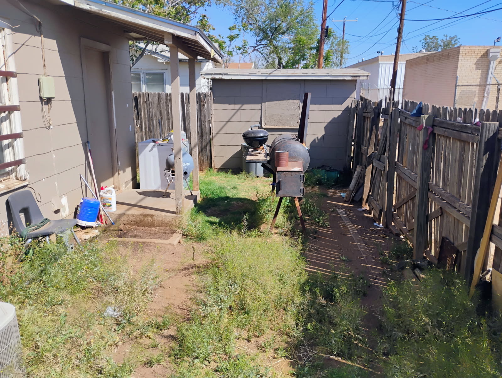 Overgrown side yard with weeds and clutter before cleanup in Lubbock, TX
