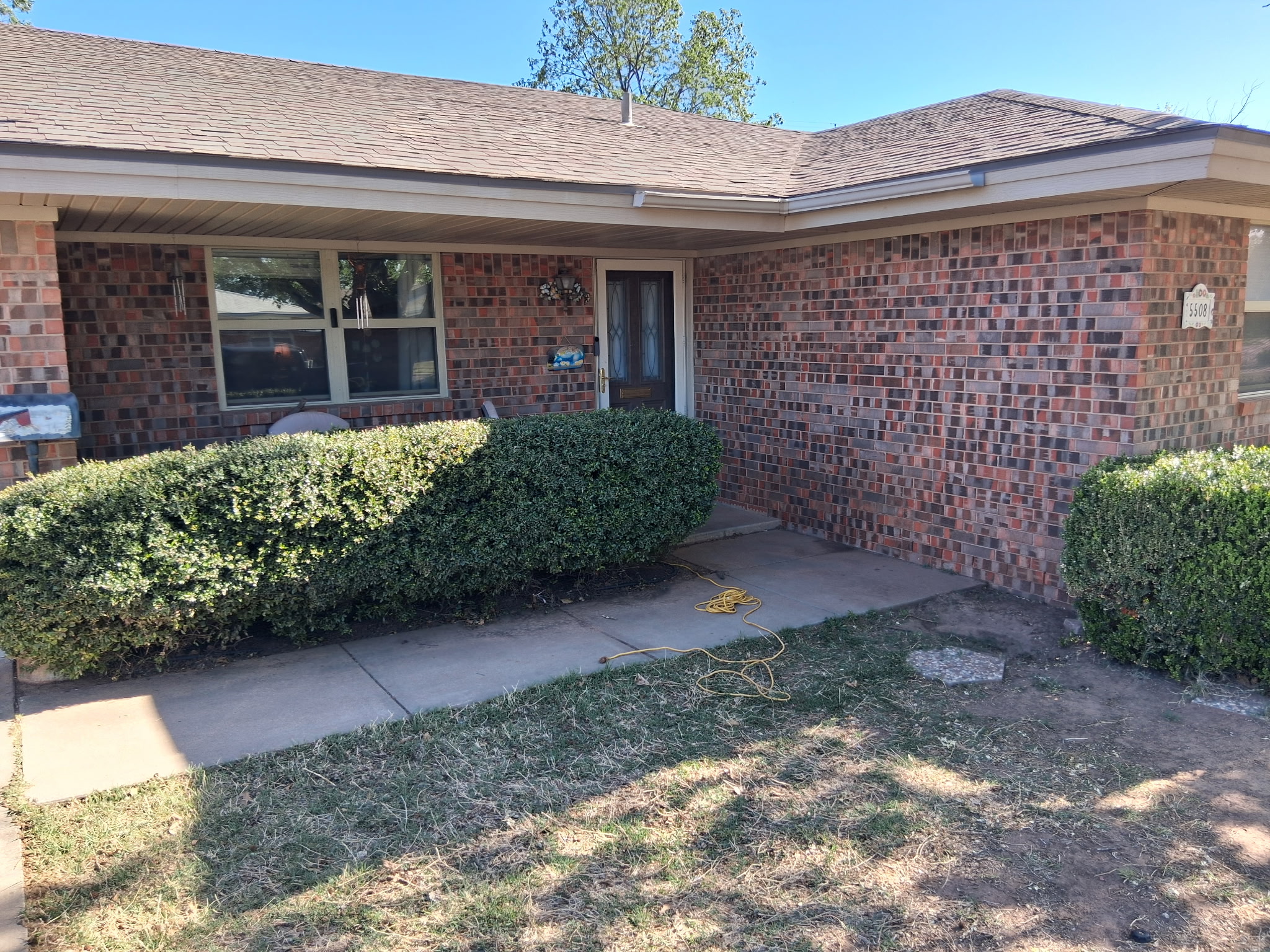 Neatly trimmed boxwood hedges at a brick home after service by 3D Landscaping in Lubbock, TX