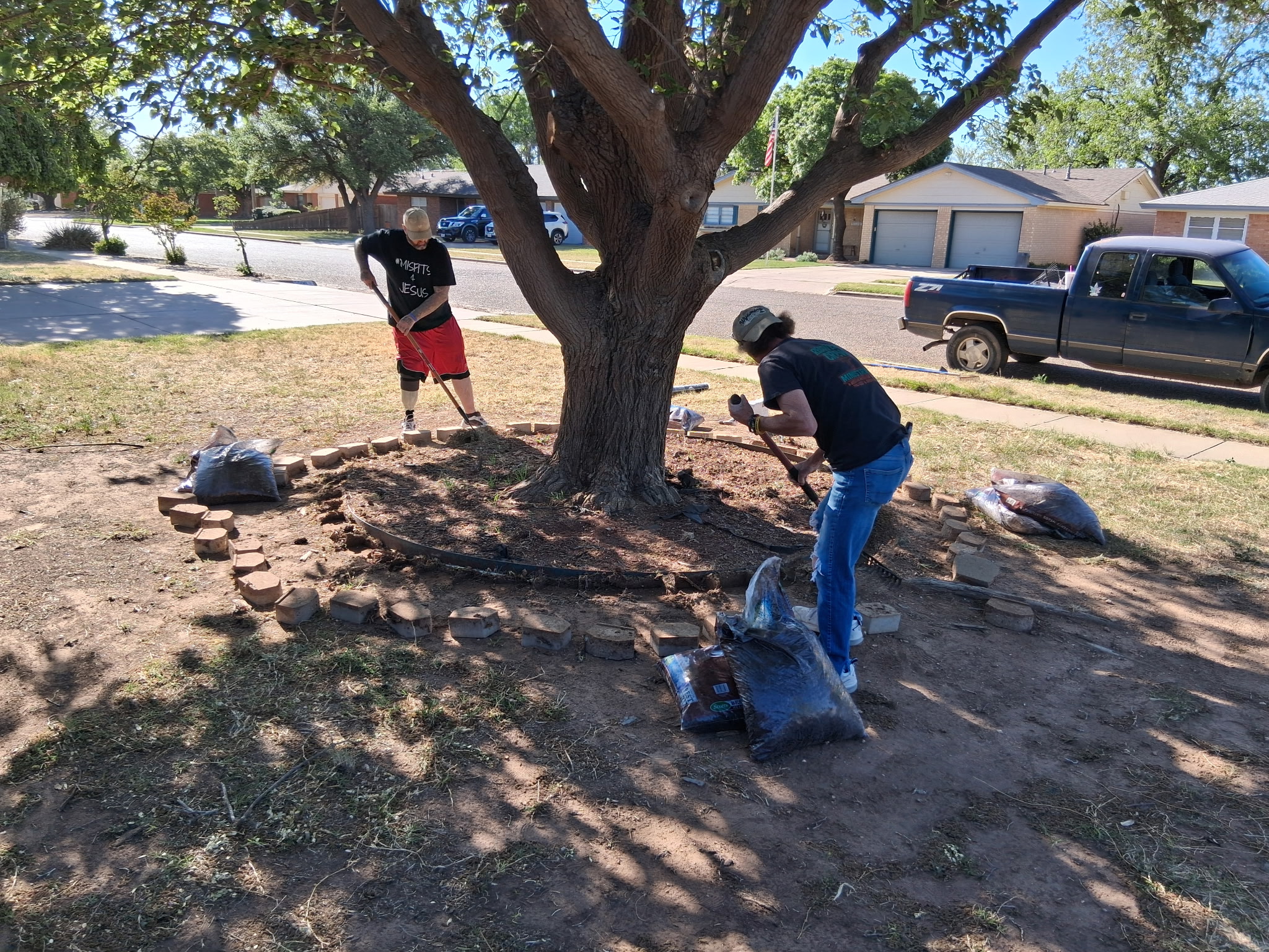 Two 3D Landscaping crew members laying stone border and mulch around a front yard tree in Lubbock, TX